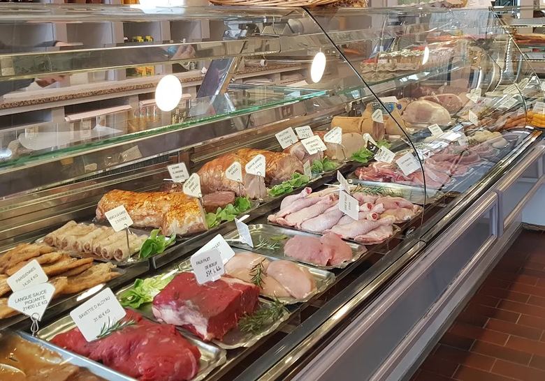 Vitrine réfrigérée de la boutique garnie de rôtis, escalopes panées, volailles et pièces de bœuf avec leurs étiquettes manuscrites