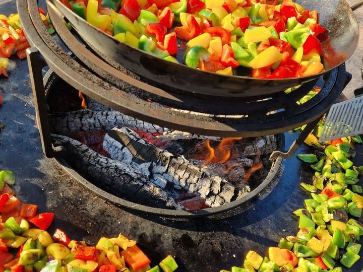 Poivrons rouges, verts et jaunes qui grillent sur la plancha d'un brasero au feu de bois