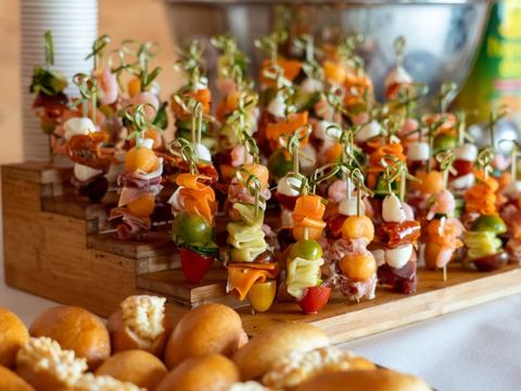Brochettes apéritives de melon, mozzarella, crevettes et charcuterie plantées sur un présentoir en bois