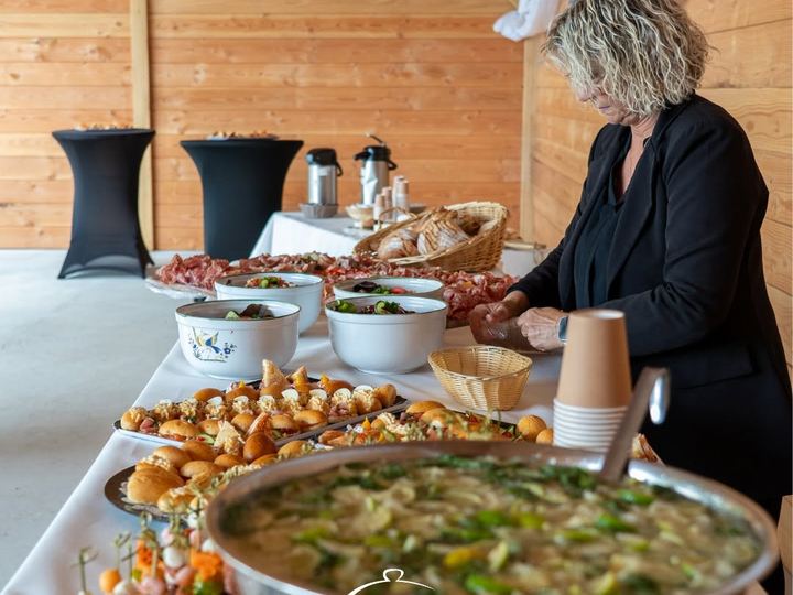 Buffet froid dressé sur nappe blanche dans une salle de réception en bois, charcuterie, salades et verrines