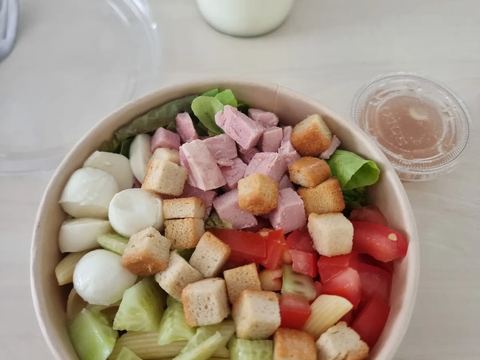 Salade repas en bol carton avec jambon, mozzarella, tomates et croûtons, accompagnée d'un yaourt en pot de verre